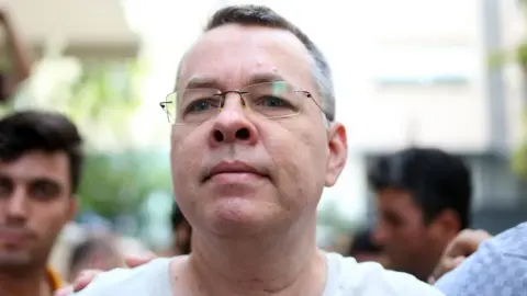 Getty Images Pastor Andrew Craig Brunson is escorted by Turkish plainclothes police officers as he arrives at his house in Izmir, Turkey, 25 July 2018