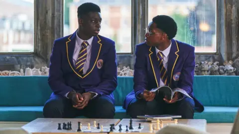 BBC/Studio Lambert Production still from BBC Three series Boarders. It shows two actors sat next to each other and talking.