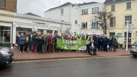 BBC The crowd gathered in Wiveliscombe with a 'Save our Buses' banner