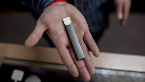 Getty Images Ryan Purington, an employee at Lucky Juju, holds a JUUL vape in his hand.