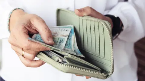 JJFarquitectos/Getty Images Woman holding wallet with money inside