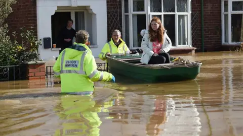 AFP via Getty Images People rescued by boat from their flooded homes in Hereford