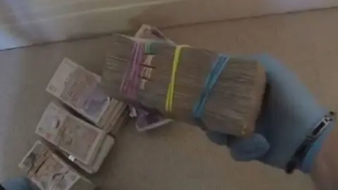 Met Police Bundles of cash in rubber bands being held by police wearing a blue rubber glove