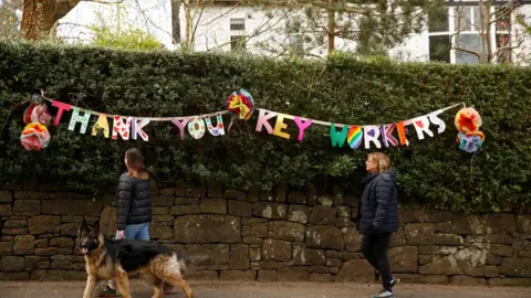 Reuters People walk past a banner reading "Thank you key workers", as the spread of the coronavirus disease (COVID-19) continues, Manchester