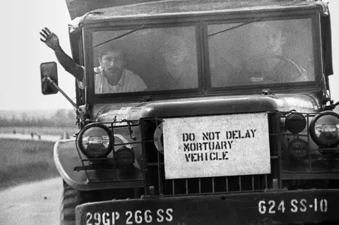 Philip Jones Griffiths/MAGNUM PHOTOS A sign on the front of a truck which reads 'do not delay mortuary vehicle'