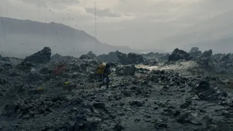 Kojima Productions A man drags a futuristic looking package across a barren, rocky landscape.