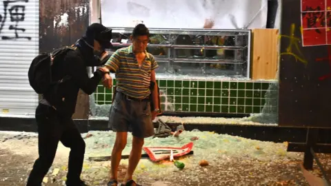 Getty Images A protester stands over broken glass in front of a vandalised shop in Hong Kong on 1 October