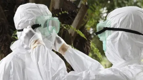 EPA Liberian nurses put on protective clothing as preparation to carry the body of an Ebola victim for burial (08 August 2014)