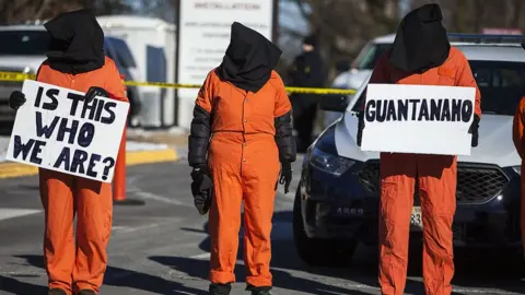 Getty Images Activists holding 'Is this who we are' sign dressed as detainee