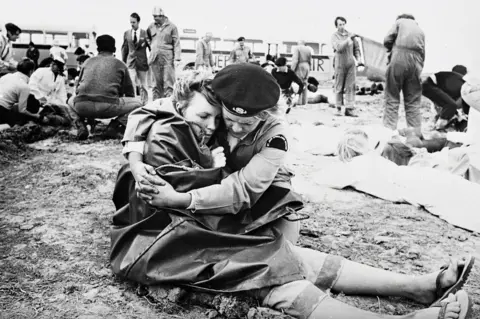 St John Ambulance A volunteer embraces a woman wrapped in a blanket