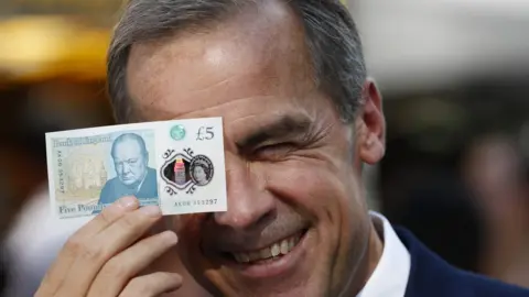 Getty Images Mark Carney poses with a new polymer five pound note in London