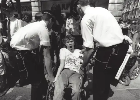 Liam Proudlock Wheelchair user being lifted by police