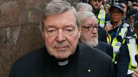 Getty Images George Pell tailed by his lawyer and a police escort at a court appearance in Melbourne in May 2018