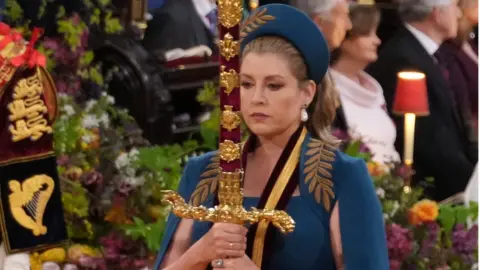 PA Media Ms Mordaunt carrying the Sword of State in the procession through Westminster Abbey
