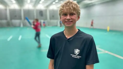BBC Matthew stands smiling at an indoor cricket court