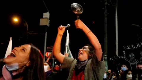 Reuters A woman bangs a pot as she reacts to the referendum on a new Chilean constitution in Valparaiso, Chile, October 25, 2020