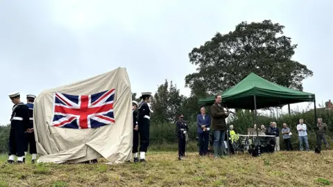 MP Darren Jones gives a speech next to the sculpture, which is covered in a drape