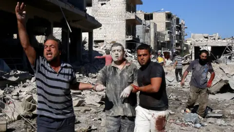 AFP An injured man is led away after an after an air strike on a market place in the opposition-held town of Maarat al-Numan, Syria (22 July 2019)