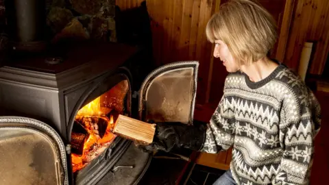 Getty Images Woman putting log in stove