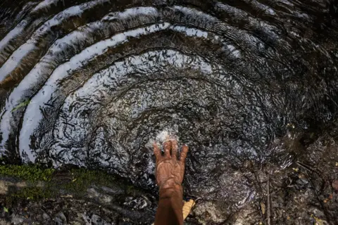 Fernanda Pineda A woman puts her hand in the river