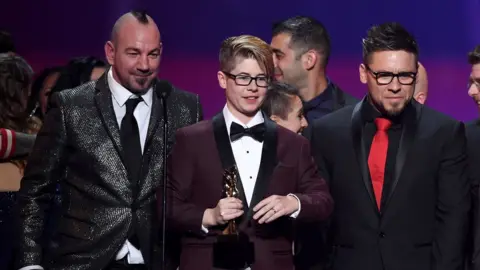 Getty Images Bree Mills (centre) accepts the award for Movie of the Year during the 2018 Adult Video News Awards, together with co-director Craven Moorehead (left) and producer Billy Visual (right)