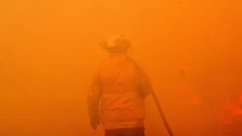 Getty Images A firefighter seen among the thick smoke and orange light of a bushfire near Sydney