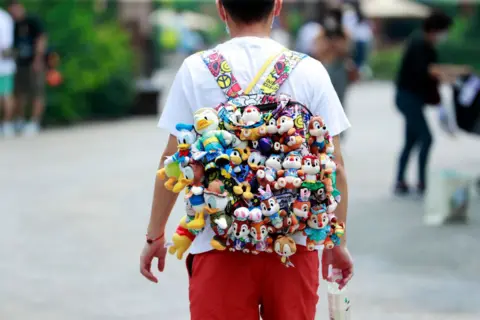 China News Service/Getty Images A visitor walks with dolls hanging from the backpack