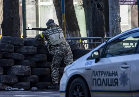 Anadolu Agency / Getty Images Ukrainian soldier stands guard behind tyres in Kyiv in Ukraine, on February 26, 2022.