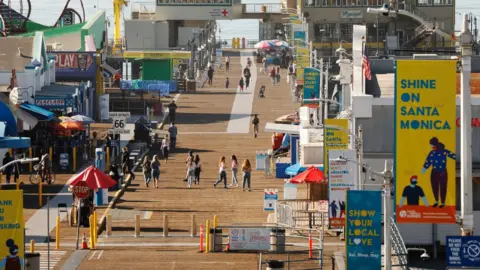 Los Angeles Times via Getty Images Pedestrians enjoy the weather on the Santa Monica Pier which has been temporarily closed January weekends