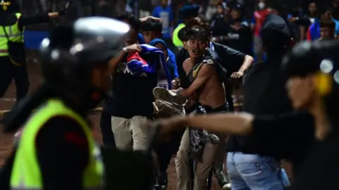 AFP via Getty Images A group of people carry a man after a football match