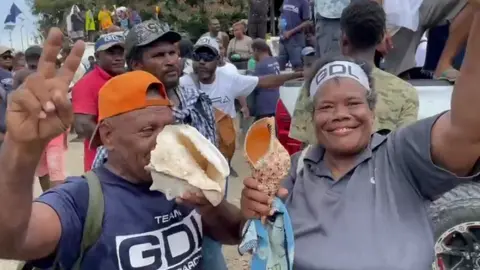 BBC MEDIA ACTION Supporters blowing through conch shells at an election day party