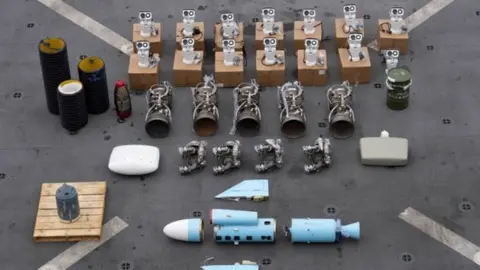 US Central Command Weapons seized by the US from a ship near the coast of Somalia, lined up on the deck of a ship. It shows a number of deconstructed parts, with a missile shown in multiple parts at the bottom of the screen.