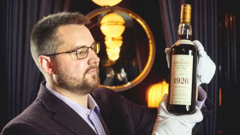 Peter Dibdin Auctioneer holding bottle of 1926 Macallan before auction