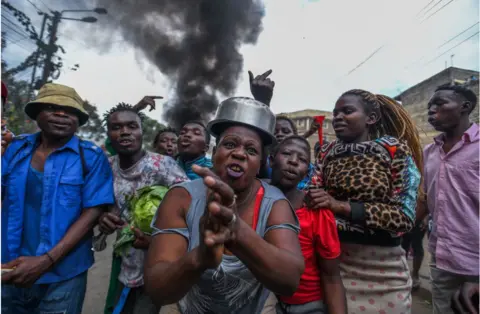 Gerald Anderson/Getty Images Animated protesters. There is smoke in the photo and someone in the middle with what looks like a cooking pot on their head.