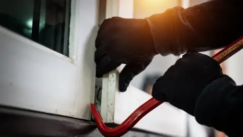 Getty Images A stock image showing a person in gloves using a crowbar to open a window to gain access to a home