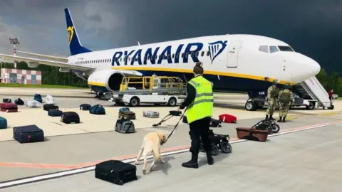 HO via EPA Belarusian security officials with with a sniffer dog checking the luggage of passengers in front of the diverted Ryanair flight at Minsk airport. Photo: 23 May 2021