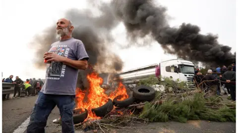 Reuters A man stands near a fire as farmers block a highway in Spain