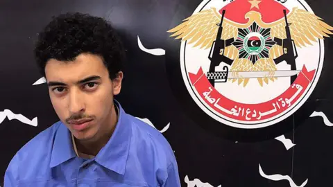 Libyan Interior Ministry Hashem Abedi is seen next to the logo of Libya's Special Deterrence Forces in a handout photo dated May 25