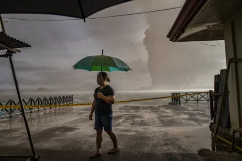Ezra Acayan A resident in Talisay walks along a lakeside as Taal Volcano erupts on January 12