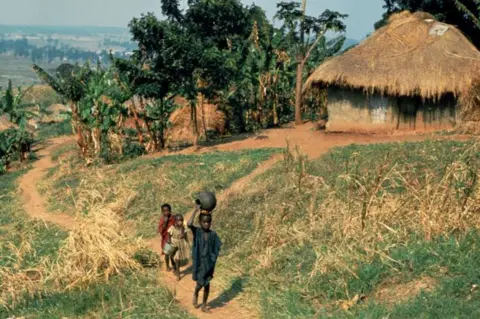 Getty Images children walking on dirt path past thatched roof house