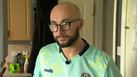 BBC Christopher Stephens, wearing a green GAA jersey and glasses, looks at the camera