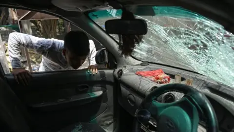 Getty Images A youth looks inside a damaged car in a residential area of Jahangirpuri in New Delhi on April 17, 2022, after clashes broke out between members of two communities on April 16 during a 'Hanuman Jayanti' religious procession.