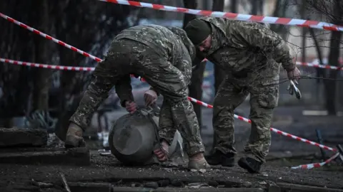 Reuters Two people in military fatigues lean over a large round metal item