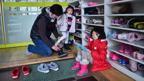 AFP South Korean father puts footwear on his son as his daughter looks on at a childcare centre in Seoul on 22 December 2015