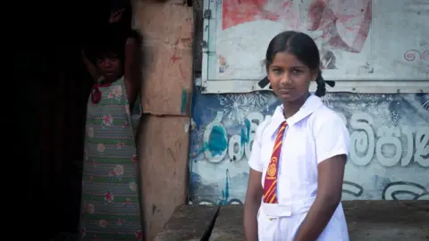 Ishara Danasekara/BBC Malki standing in front of her home