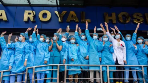 Getty Images Hospital health workers make the three finger salute during a demonstration against the military coup. A massive crowd took to the streets of Yangon for the second day of protest against the coup and demanded the release of Aung San Suu Kyi as the government cut off the internet.