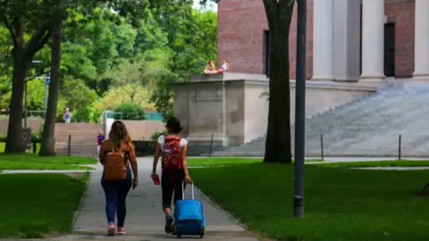 NurPhoto via Getty Images wo students are seen leaving their campus with baggage at Harvard University premises in Cambridge