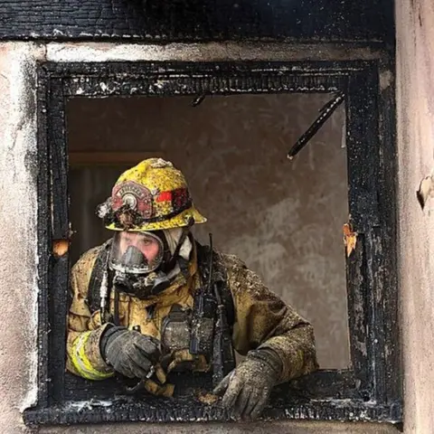 IAFF a firefighter leans out of a burnt door frame