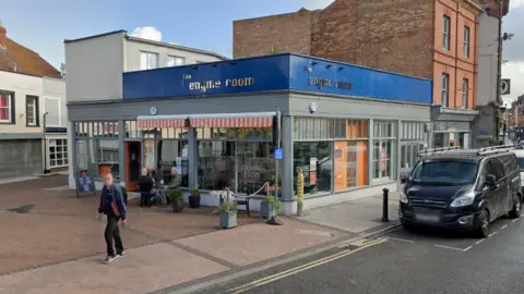 LDRS A single storey building with big window frontage on two sides, and blue backed signs above which say the engine room, some cafe tables and chairs outside the door