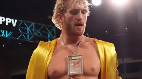 Getty Images Logan Paul, YouTuber, wrestler and boxer, wears a diamond encrusted Pokemon card around his neck and a yellow silk robe drapped on his shoulders